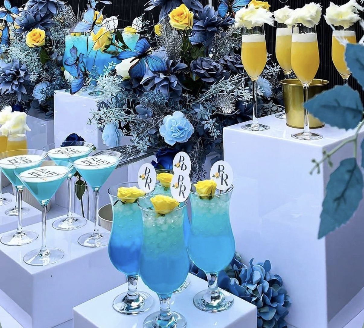 Blue and yellow baby shower beverage display with mimosas and signature cocktails