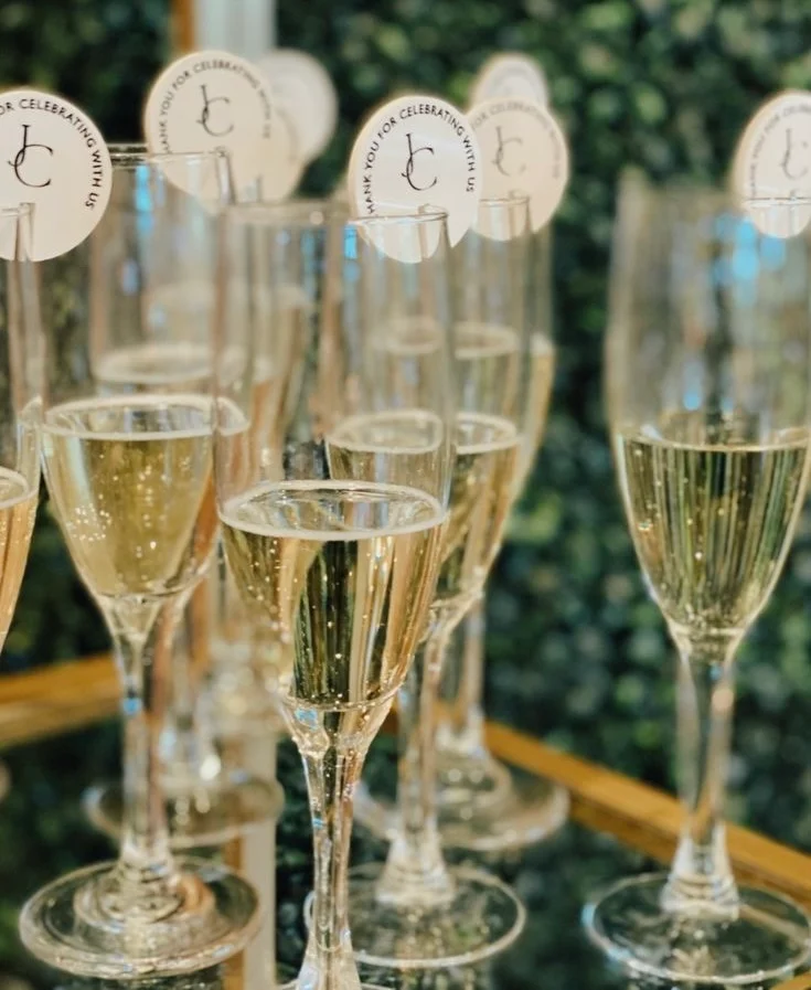 Champagne flutes with personalized thank-you tags on a mirrored tray