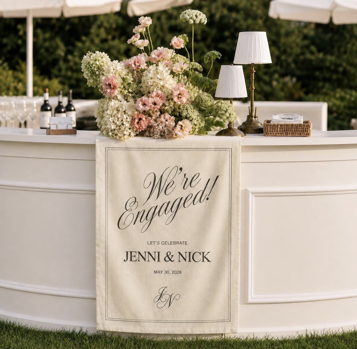 White bar with blush florals, gold lamps and a We're Engaged linen sign